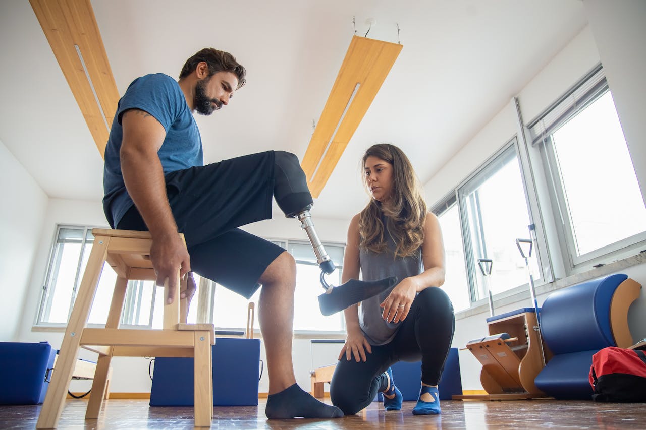 A man with a prosthetic leg assisted by a therapist during rehabilitation indoors.